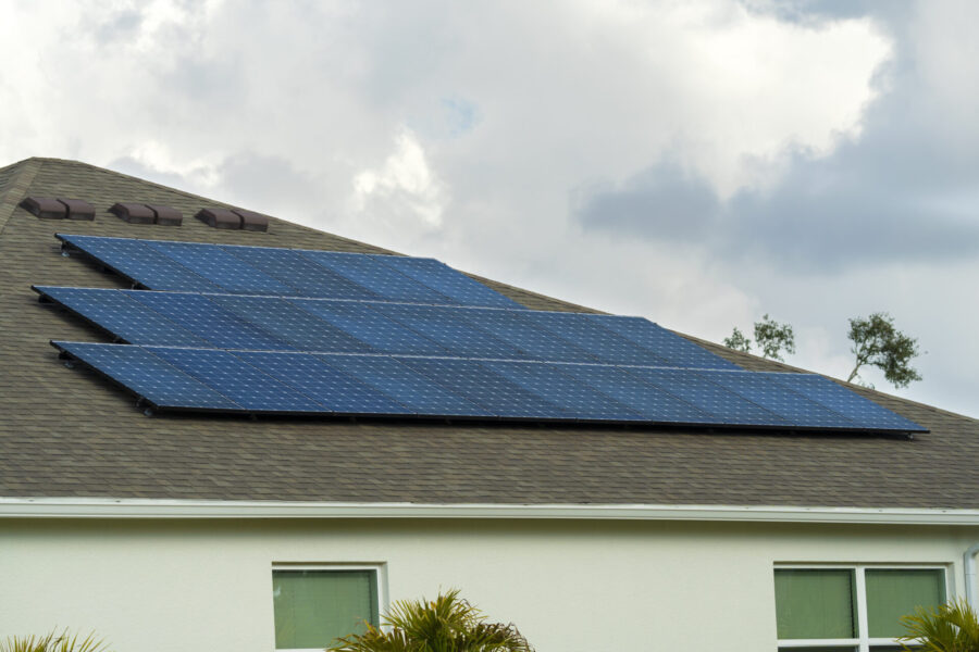 Ordinary residential house in USA with roof covered with solar panels for producing of clean ecological electricity in suburban rural area. Concept of investing in autonomous home for energy saving